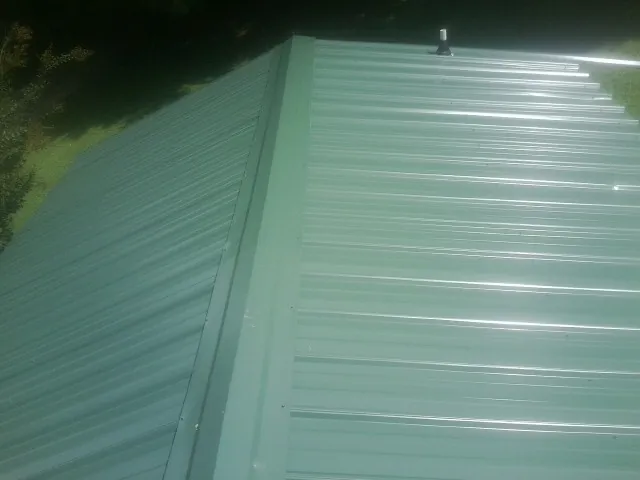 New green metal panels meeting at the ridge of a roof — Flat Roof Repair work by our crew in Winter Haven